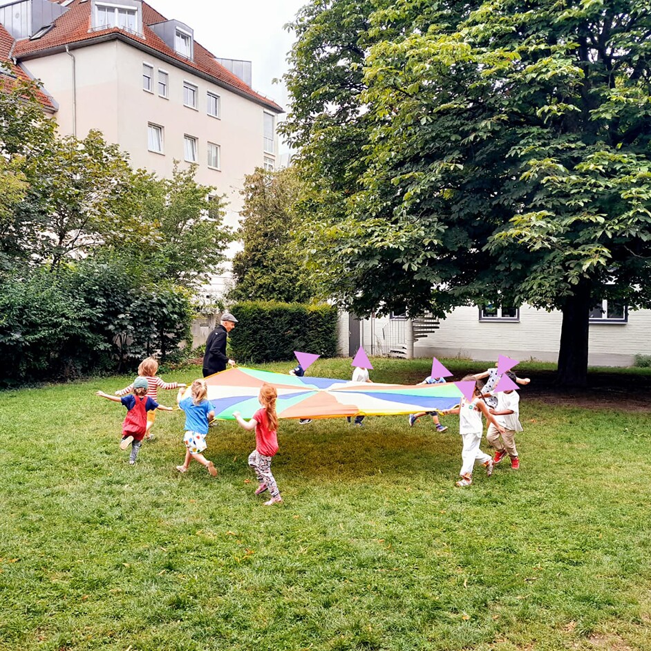 Kinder spielen mit einem bunten Schwungtuch auf einer Wiese